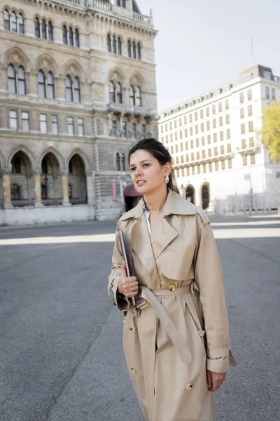 Freelancer in beige trench coat walking with laptop on street of vienna — Stock Photo