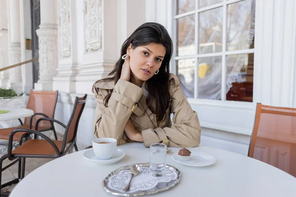 Mujer bonita en pendientes de aro mirando a la cámara en la terraza de la cafetería - foto de stock