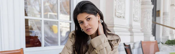 Jolie femme en cerceau boucles d'oreilles regardant caméra en terrasse café, bannière — Photo de stock