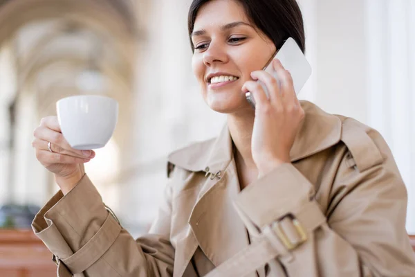 Mujer alegre sosteniendo taza y hablando en el teléfono inteligente en la terraza de verano - foto de stock