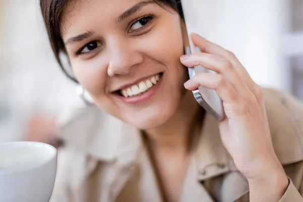 Mujer alegre sosteniendo taza y hablando en el teléfono inteligente - foto de stock