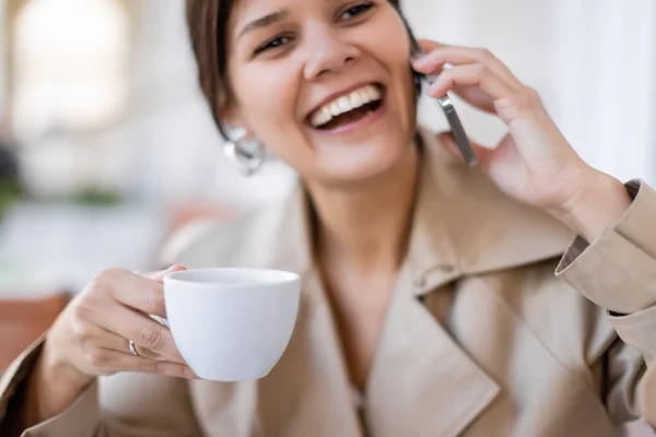 Счастливая женщина держит чашку и разговаривает по смартфону на летней террасе — стоковое фото