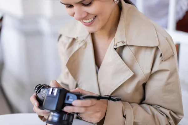 Heureux photographe en trench coat regardant appareil photo numérique — Photo de stock