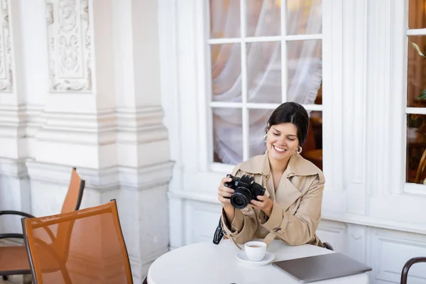 Fotógrafo feliz en gabardina mirando a la cámara digital - foto de stock