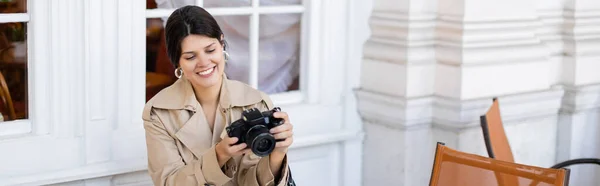 Glücklicher Fotograf im Trenchcoat mit Blick auf Digitalkamera, Banner — Stockfoto