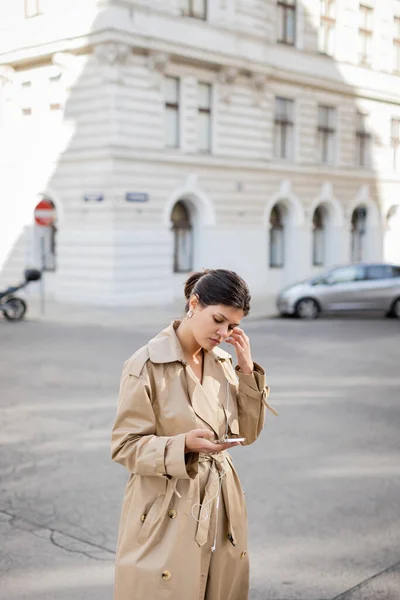 Mulher usando fones de ouvido com fio segurando telefone celular e ouvindo música na rua em Viena — Fotografia de Stock