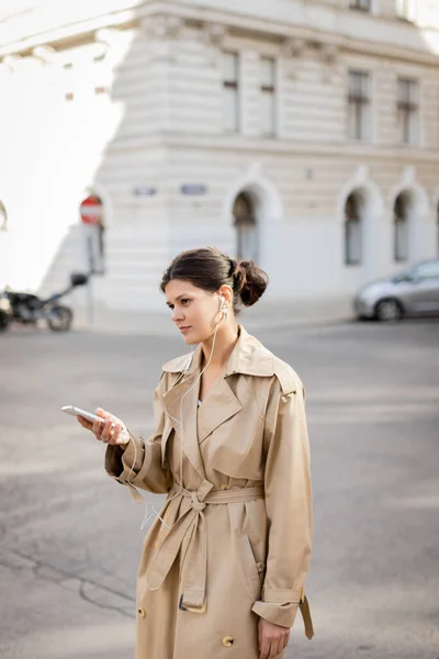Woman in wired earphones holding mobile phone and listening music on street in vienna — Stock Photo