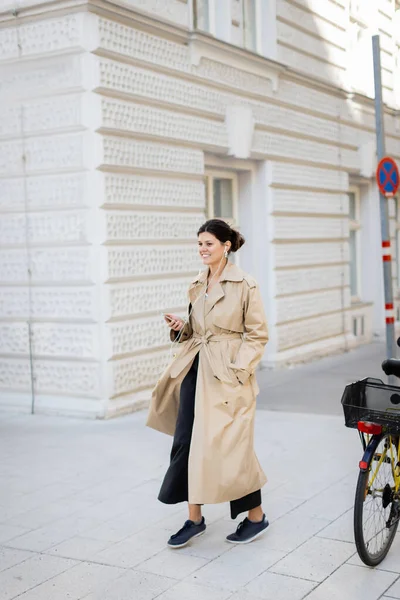 Femme gaie dans les écouteurs tenant téléphone portable et écouter de la musique dans la rue à Vienne — Photo de stock