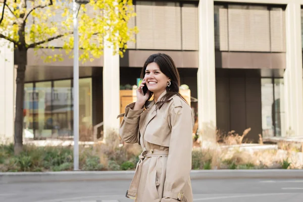 Happy woman in beige coat talking on smartphone on street of vienna — Stock Photo
