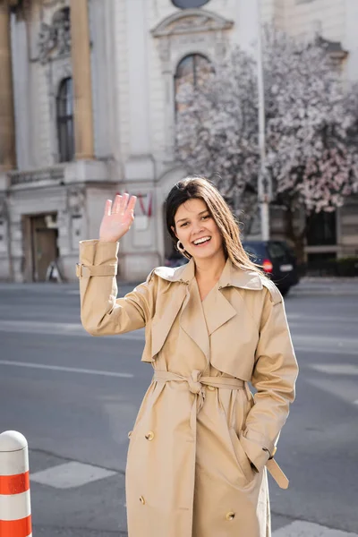 Donna felice in elegante cappotto sorridente e agitando mano sulla strada a Vienna — Foto stock