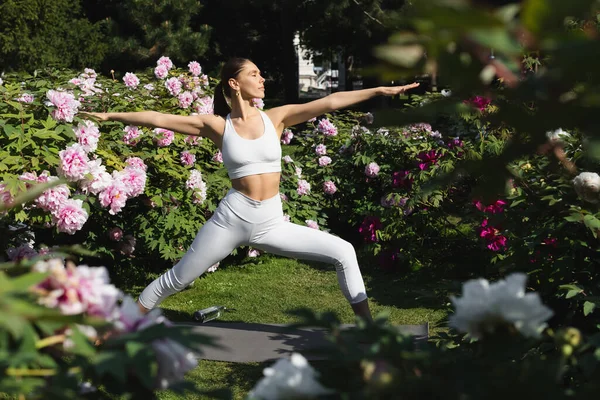 Slender woman with closed eyes and outstretched hands meditating in warrior pose in park — Foto stock