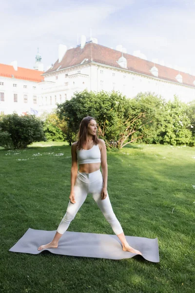 Sportive woman in white sports bra and leggings standing in tree pose on yoga mat — Stockfoto