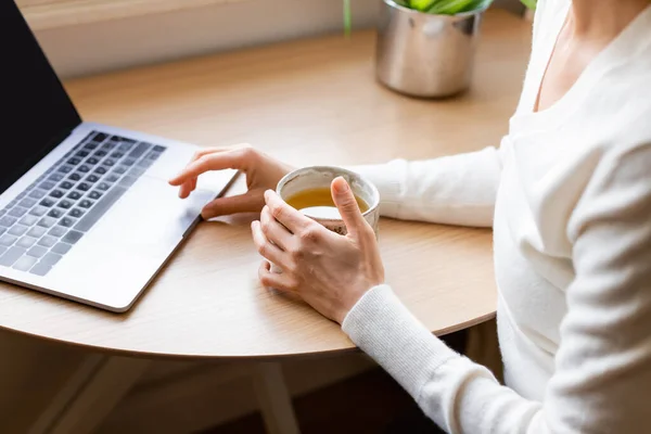 Cropped view of woman with clay cup sitting near blurred laptop at home — Foto stock