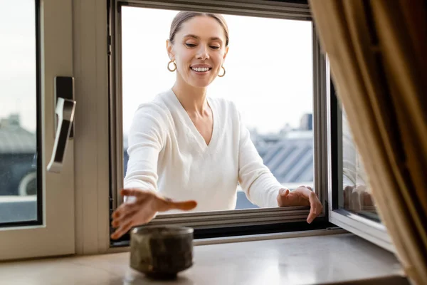 Cheerful woman reaching blurred tea cup on windowsill at home — Foto stock