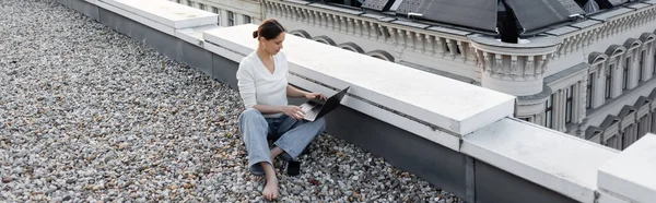 High angle view of barefoot woman working on laptop on rooftop, banner — Fotografia de Stock