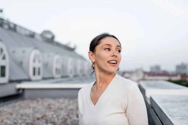 Glückliche Frau im weißen Pullover, die auf dem Dach wegschaut — Stockfoto