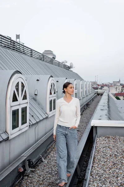 Full length of barefoot woman walking with hand in pocket on rooftop — стоковое фото