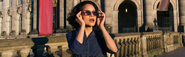 Stylish young woman wearing sunglasses near building on museum island, banner — Photo de stock