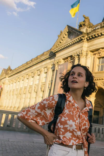 Здивована молода жінка у сонцезахисних окулярах стоїть біля бод - музею з прапором українки. — стокове фото
