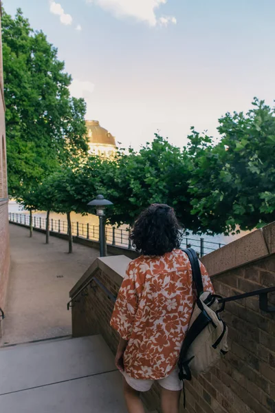 Back view of curly woman walking on stairs with backpack — Stock Photo