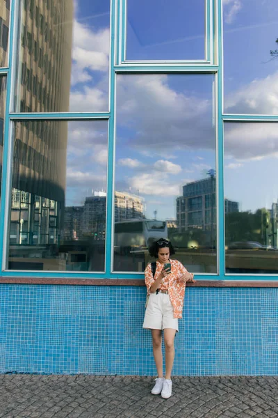 Curly young woman chatting on smartphone near building in berlin — Photo de stock