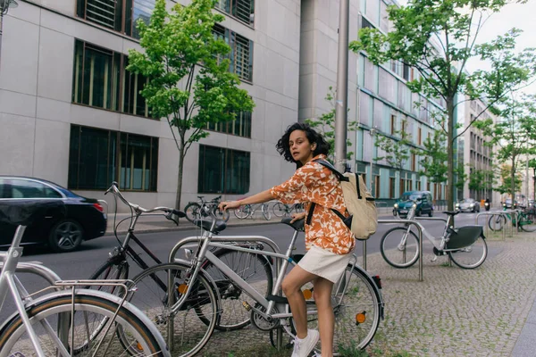 Full length of curious young woman in summer outfit standing near bicycle in berlin — Foto stock