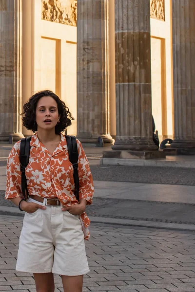 Amazed traveler with backpack standing with hands in pockets near ancient columns — Photo de stock
