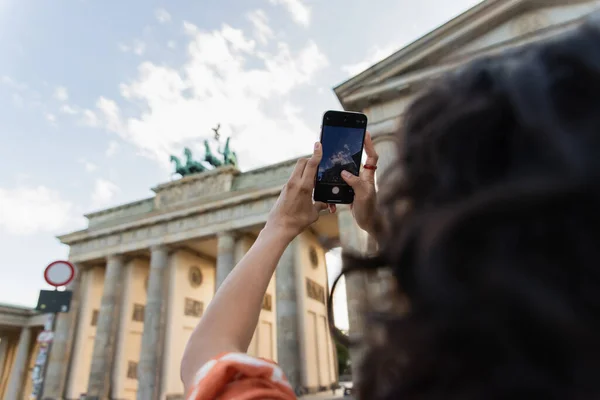 Blurred and curly tourist taking photo of brandenburg gate in berlin — Stock Photo