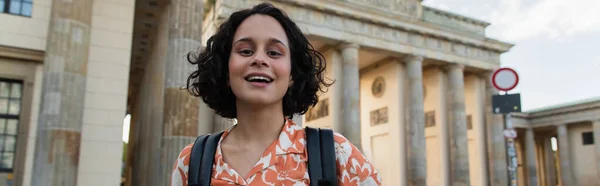 Cheerful tourist with backpack standing near brandenburg gate in berlin, banner - foto de stock