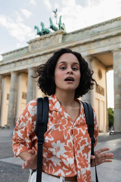 Surprised young tourist with backpack standing near brandenburg gate in berlin — Photo de stock