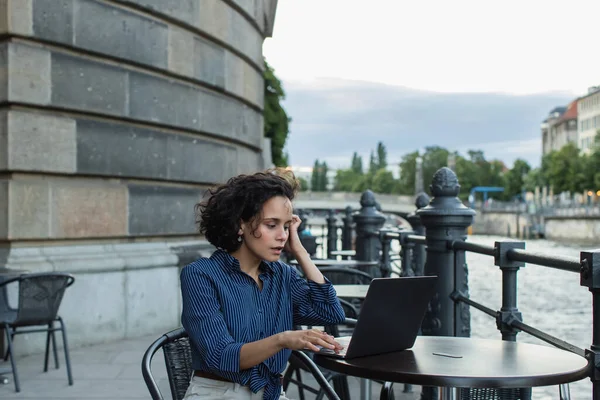 Surprised young freelancer using laptop while sitting on summer terrace near river in berlin - foto de stock