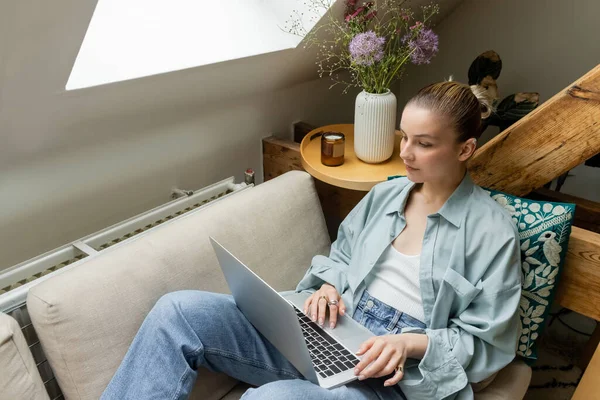 Junge Frau benutzt Laptop, während sie zu Hause auf der Couch sitzt — Stockfoto