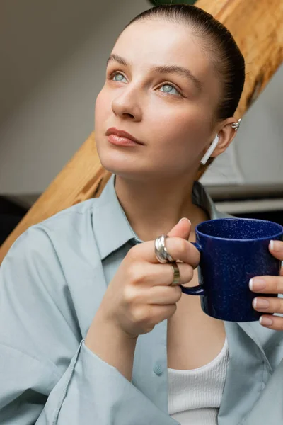 Portrait of young woman in earphone holding cup at home — Stock Photo