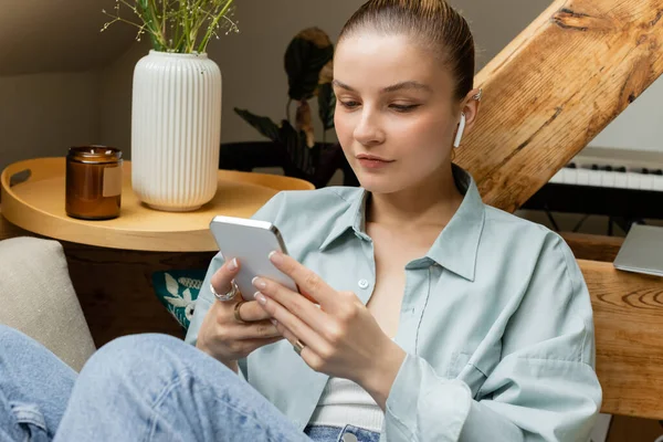 Woman in earphone using cellphone on couch in living room — Stock Photo