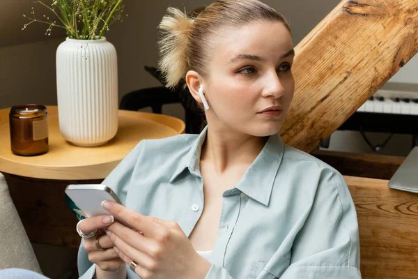 Young woman in earphone holding smartphone in living room — Stock Photo