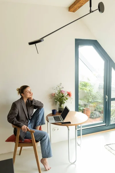 Freelancer en chaqueta sentado cerca de aparatos y taza en casa - foto de stock