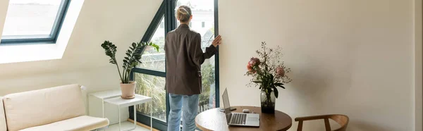 Back view of woman standing near balcony door and devices on table at home, banner — Stock Photo