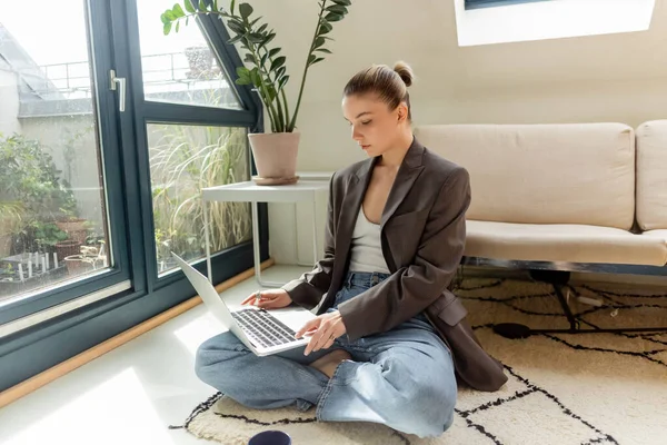 Freelancer em blazer usando laptop enquanto sentado no tapete em casa — Fotografia de Stock