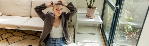 Freelancer in jacket touching hair near laptop in living room, banner — Stock Photo