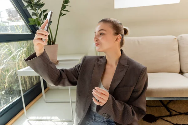 Femme souriante prenant selfie sur smartphone dans le salon — Photo de stock