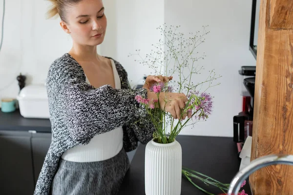 Donna in cardigan lavorato a maglia che mette fiori in vaso in cucina — Foto stock