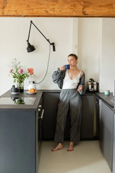 Donna in maglia cardigan tenendo tazza in cucina moderna a casa — Foto stock