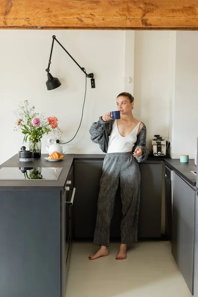 Mujer en punto cárdigan celebración taza en la cocina moderna en casa - foto de stock