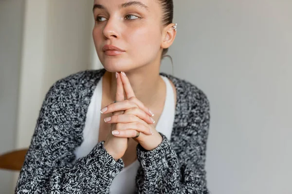 Young dreamy woman in knitted cardigan looking away at home — Stock Photo