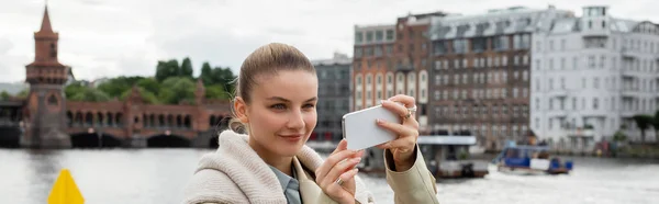 Feliz joven mujer tomando fotos en el teléfono inteligente en la calle en Berlín, pancarta - foto de stock