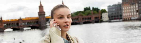 Young woman in trench coat talking on smartphone in berlin, banner — Stock Photo
