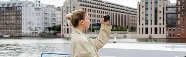 Vue latérale de la femme en trench coat prenant des photos sur téléphone portable à Berlin, bannière — Photo de stock