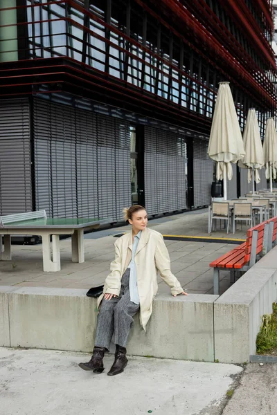 Stylish traveler in trench coat looking away near building on street in Germany — Stock Photo