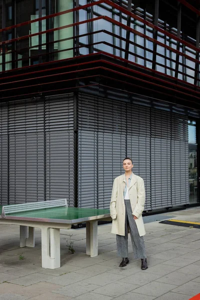 Elegante donna in trench in piedi vicino a tavolo da ping-pong all'aperto a Berlino — Foto stock