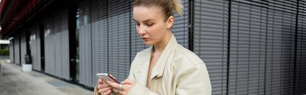 Woman in trench coat using cellphone on urban street, banner — Stock Photo